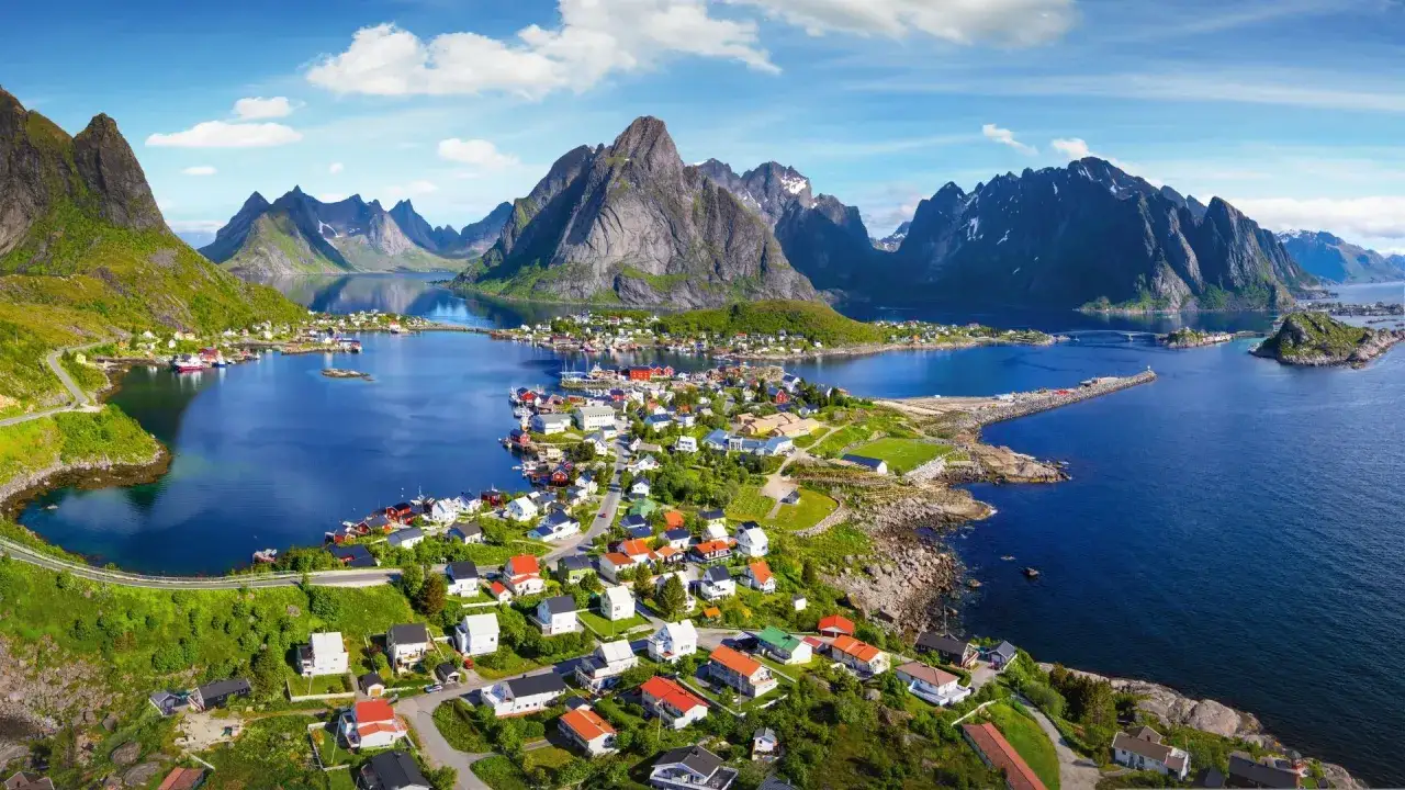 En pittoresk norsk by med färgglada hus vid en blå fjord, omgiven av dramatiska berg. En av många norge sevärdheter.