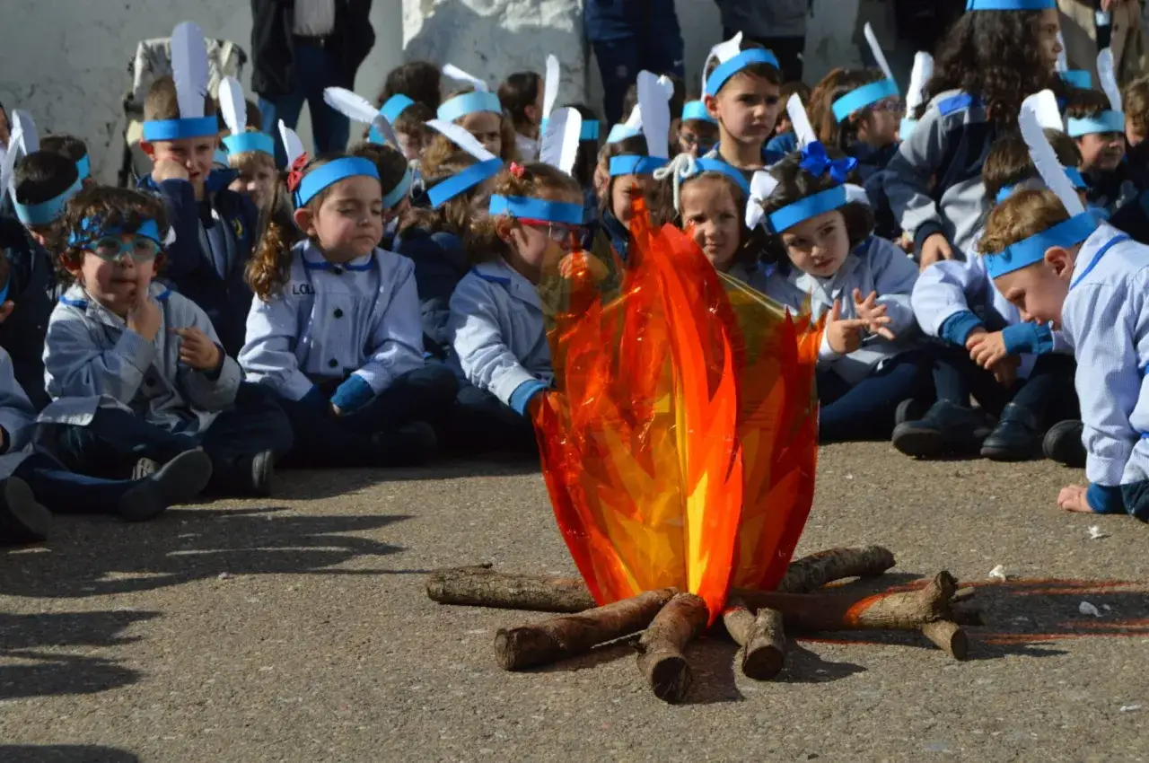 Ni&ntilde;os con plumas en la cabeza celebran un d&iacute;a de la paz para ni&ntilde;os, sentados alrededor de una fogata artificial.