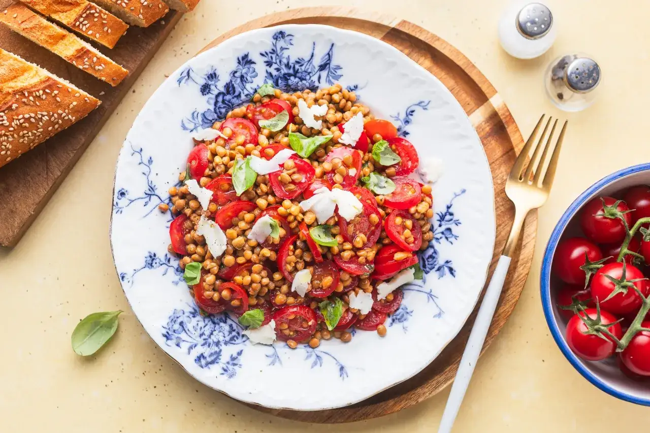 Un'insalata di lenticchie estiva con pomodorini, basilico e scaglie di formaggio, servita su un piatto decorato.