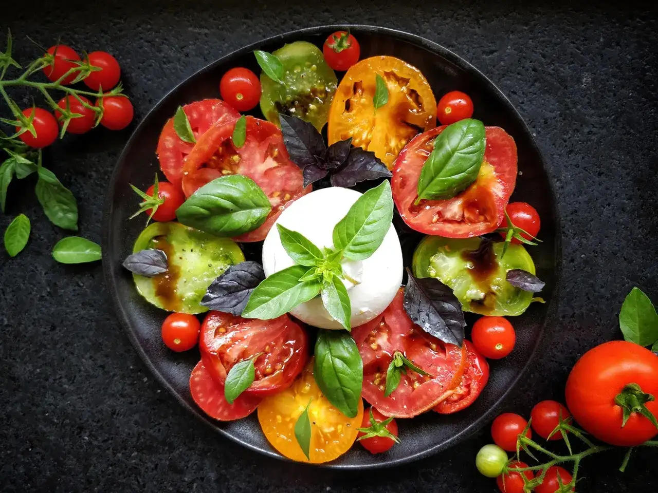 Une assiette gastronomique de tomate burrata, avec des tomates de différentes couleurs, de la burrata crémeuse et du basilic frais.