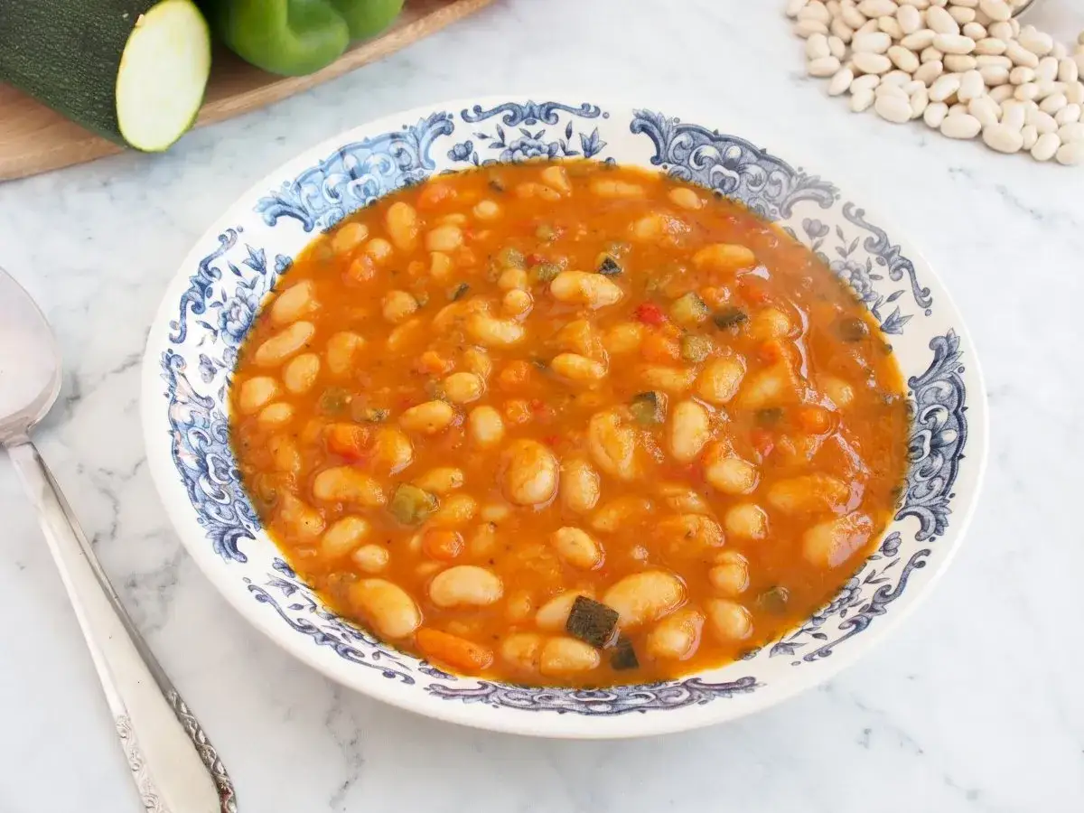 Un plato de alubias con verduras, con trozos de calabac&iacute;n y pimiento, servido en una vajilla azul y blanca.