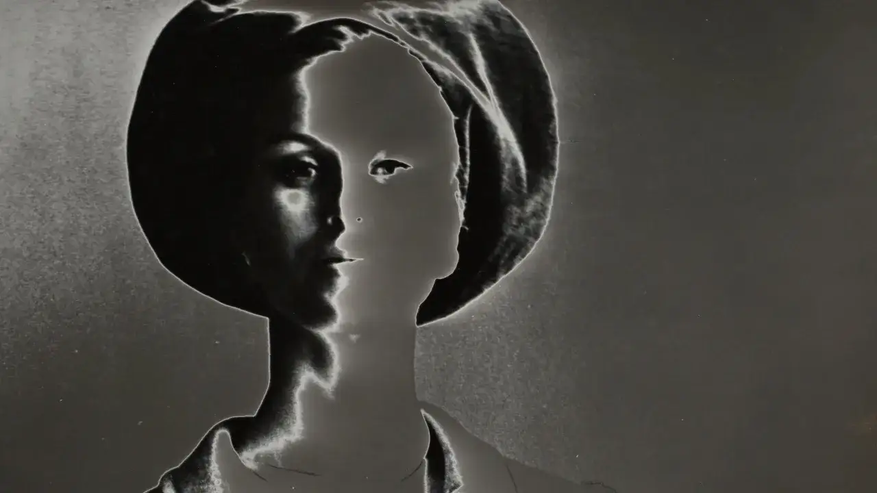 Volto femminile in primo piano, con un cappello, in stile Lillian Bassman. Luce e ombra creano un effetto etereo e misterioso.
