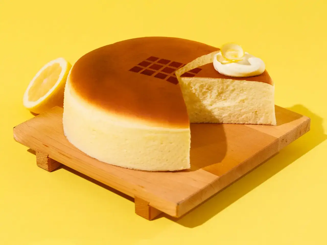 Un soffice cheesecake giapponese, con una fetta tagliata, guarnito con panna e limone, accanto a spicchi di limone fresco su un tagliere di legno.