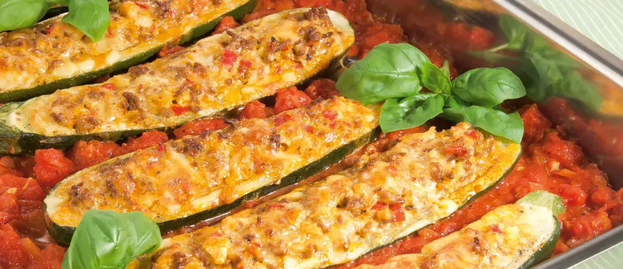 Gef&uuml;llte zucchini schiffchen mit K&auml;se &uuml;berbacken, serviert in einer Tomatensauce, garniert mit frischem Basilikum.