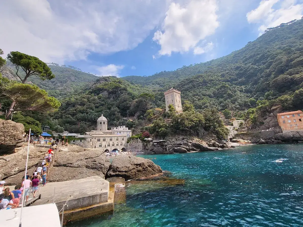 Ein versteckter geheimtipp italien strand mit kristallklarem Wasser, einer alten Abtei und einem Turm. Menschen steigen von einem Boot auf eine Treppe.
