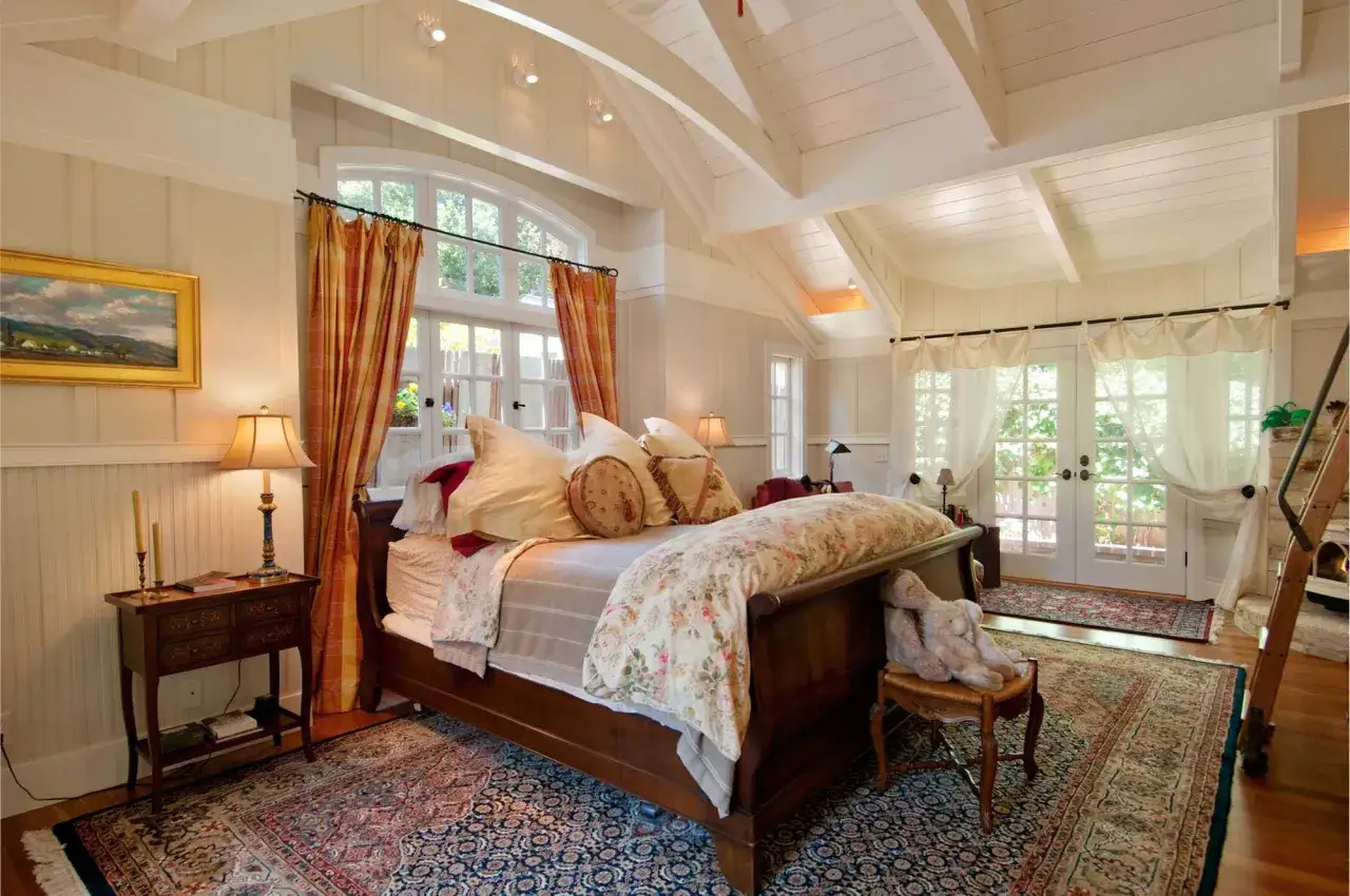 A cozy bedroom with a wooden bed against a large window, adorned with floral bedding and warm curtains.