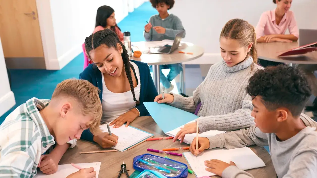Kinder arbeiten konzentriert an einem Tisch zusammen. Sie schreiben und tauschen sich aus – ein Beispiel für kooperatives Lernen.