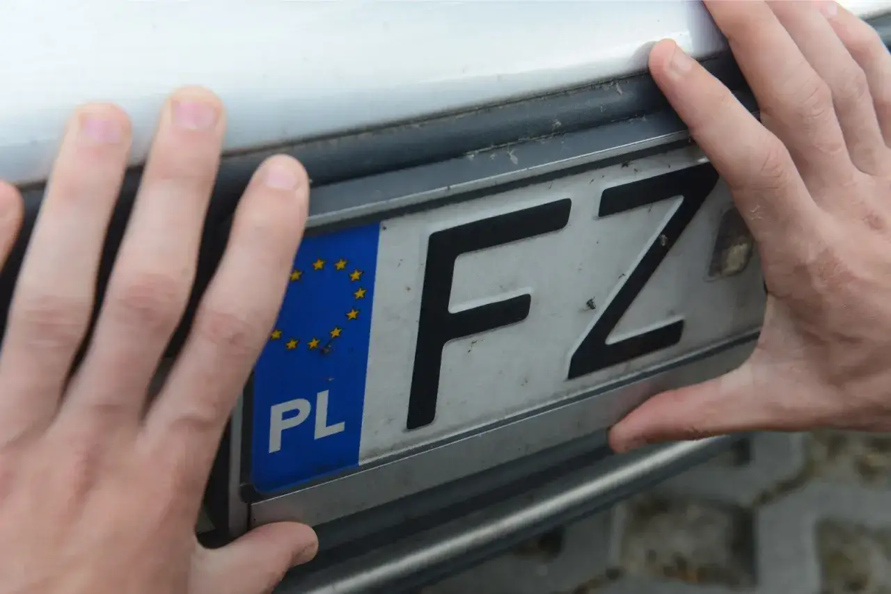 Dłonie trzymają tablicę rejestracyjną z oznaczeniem FZ.