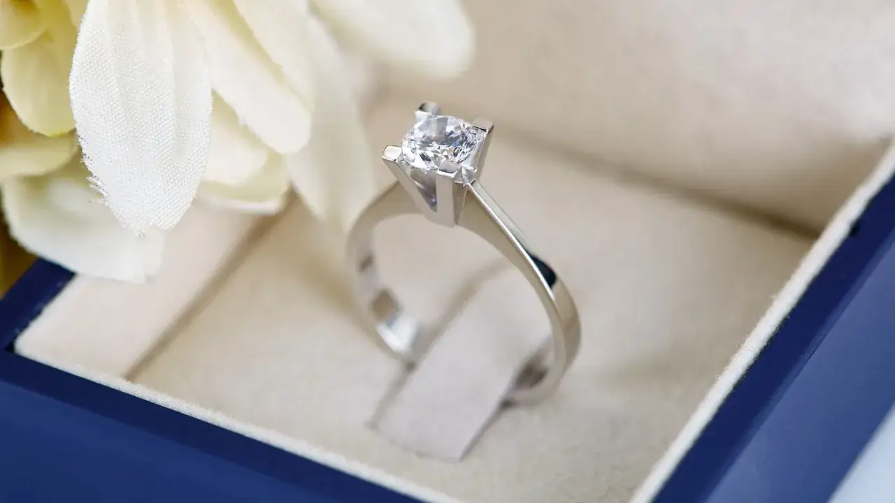 Anello con diamante solitario in oro bianco, un gioiello prezioso in una scatola blu, pronto per un'occasione speciale.
