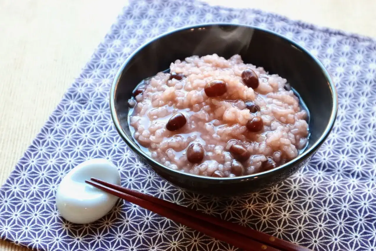 A bowl of pink rice recipe with red beans, served with chopsticks on a patterned cloth.