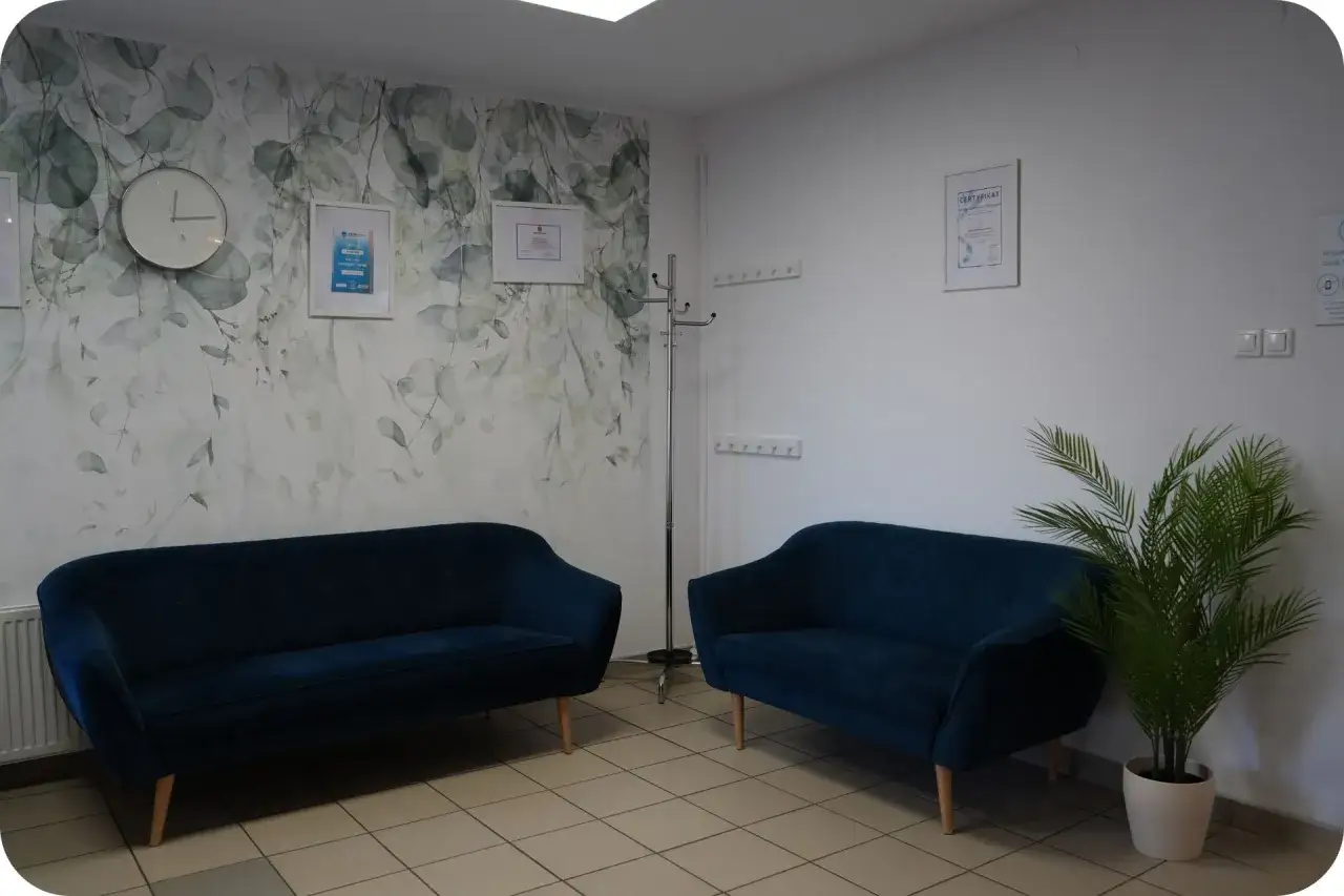 Przytulne wnętrze gabinetu, gdzie terapeuta tworzy bezpieczną przestrzeń. Dwa granatowe fotele, kwiat i dekoracje na ścianie.