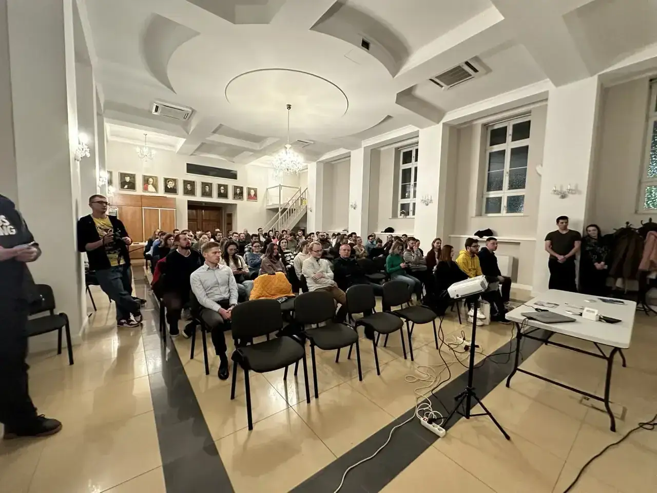 Uczestnicy słuchają wykładu, który jest częścią zajęć z samorozwoju. W sali zgromadziło się wielu młodych ludzi.