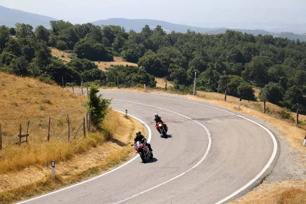 Due motociclisti affrontano una curva sul passo dello Spino, tra colline verdi e un cielo limpido.