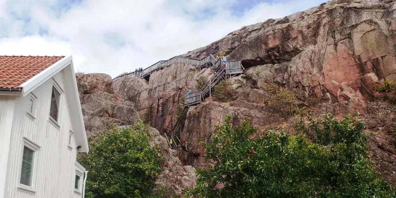 Trä trappor klättrar uppför Vetteberget i Fjällbacka, med en vit byggnad i förgrunden.