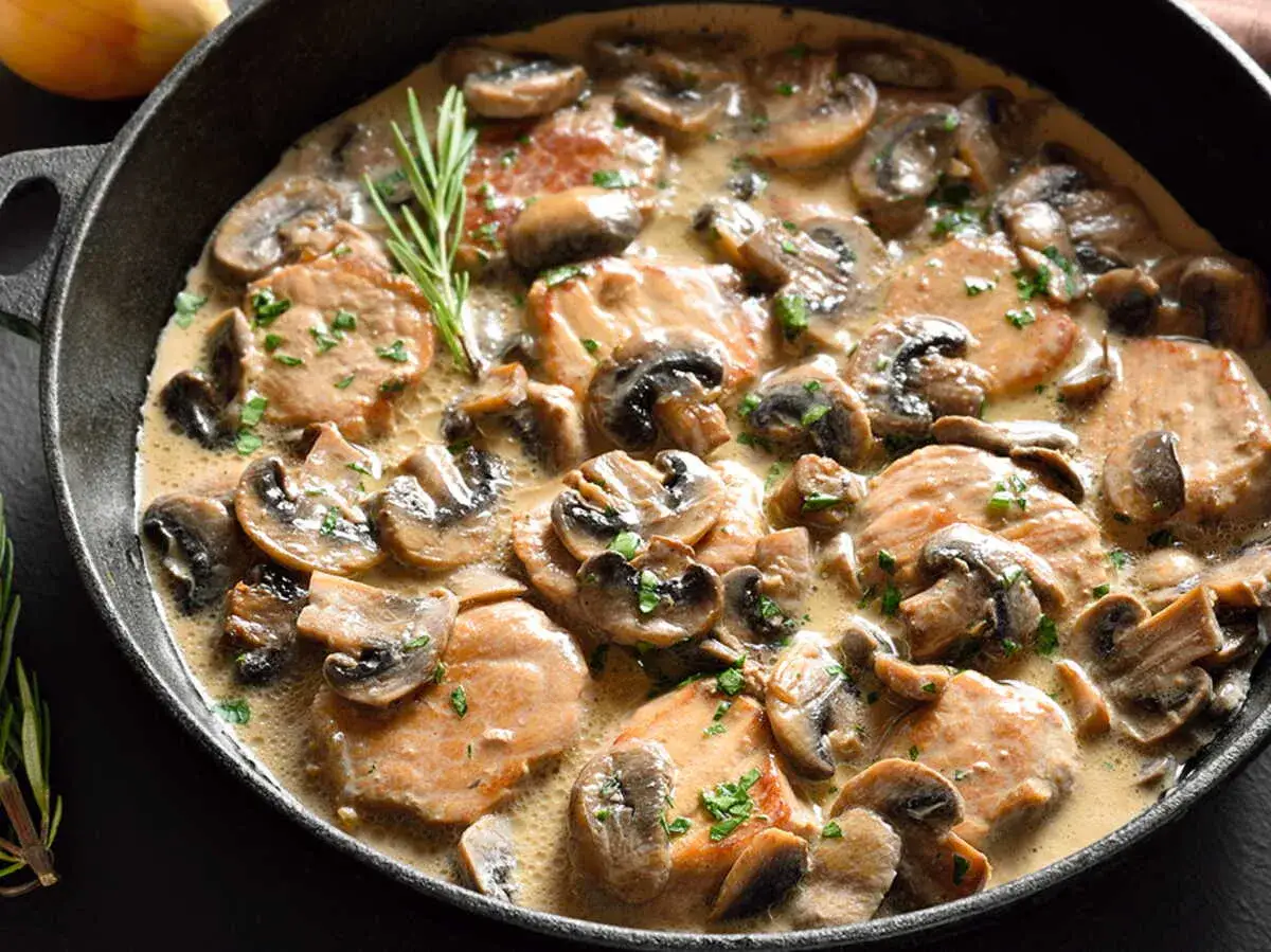 Délicieux sauté de porc champignon en sauce crémeuse, garni de persil frais et d'une branche de romarin.