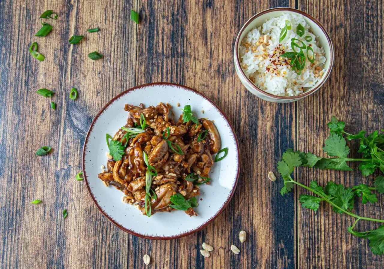 Pyszny kurczak kung pao z orzeszkami ziemnymi i ryżem, ozdobiony szczypiorkiem i kolendrą.