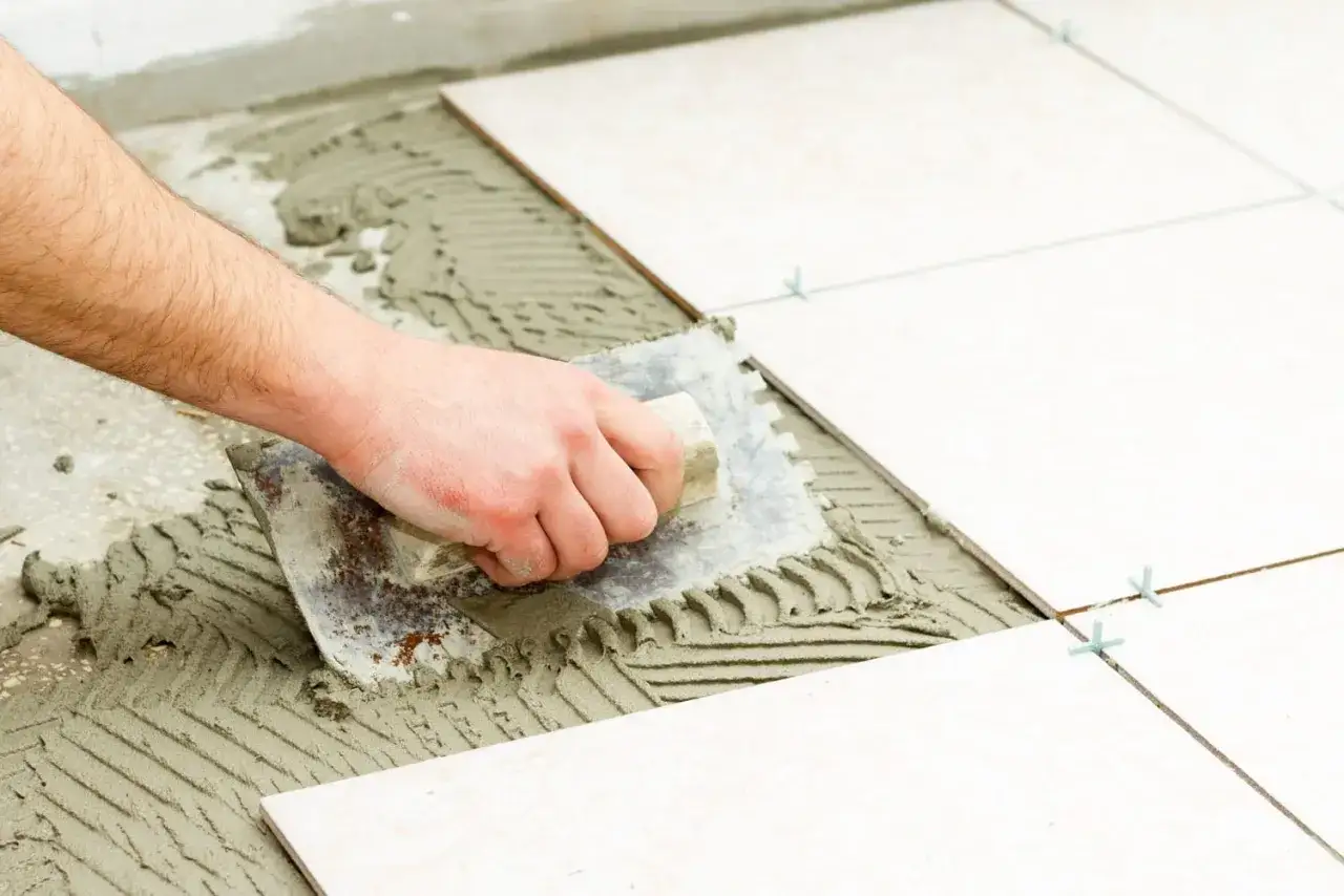 Main tenant pose la colle pour carrelage avec une truelle crant&eacute;e. La pose de carrelage est en cours.