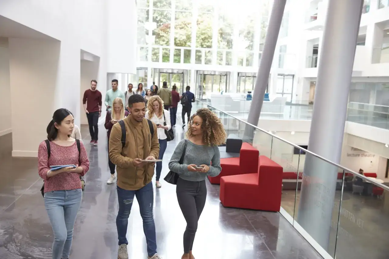 &Eacute;tudiants diversifi&eacute;s dans un hall moderne, discutant et se d&eacute;pla&ccedil;ant. Un groupe se dirige vers une grande verri&egrave;re, symbolisant l'ouverture et la **relation internationale etude**.
