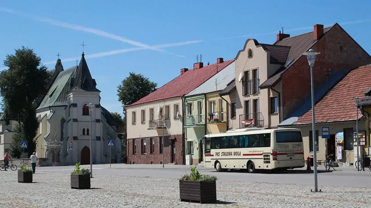 Rynek w Nowym Korczynie z kościołem i kolorowymi kamieniczkami. Autobus PKS Stalowa Wola czeka na pasażerów. To jedne z wielu atrakcji tego miejsca.