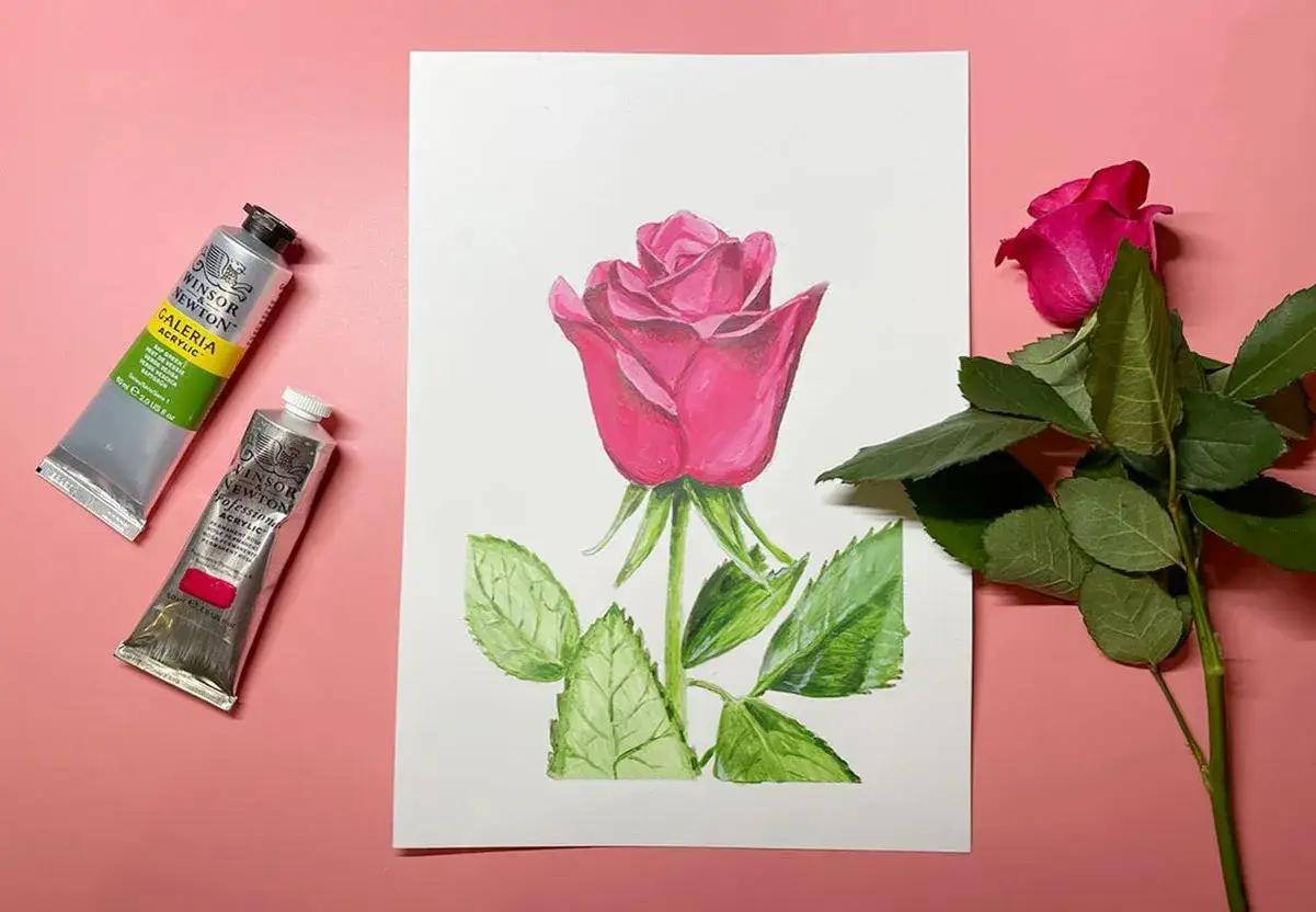 Une rose rose peinte avec des tubes de peinture à proximité. Une vraie rose rose est posée à côté de la peinture.