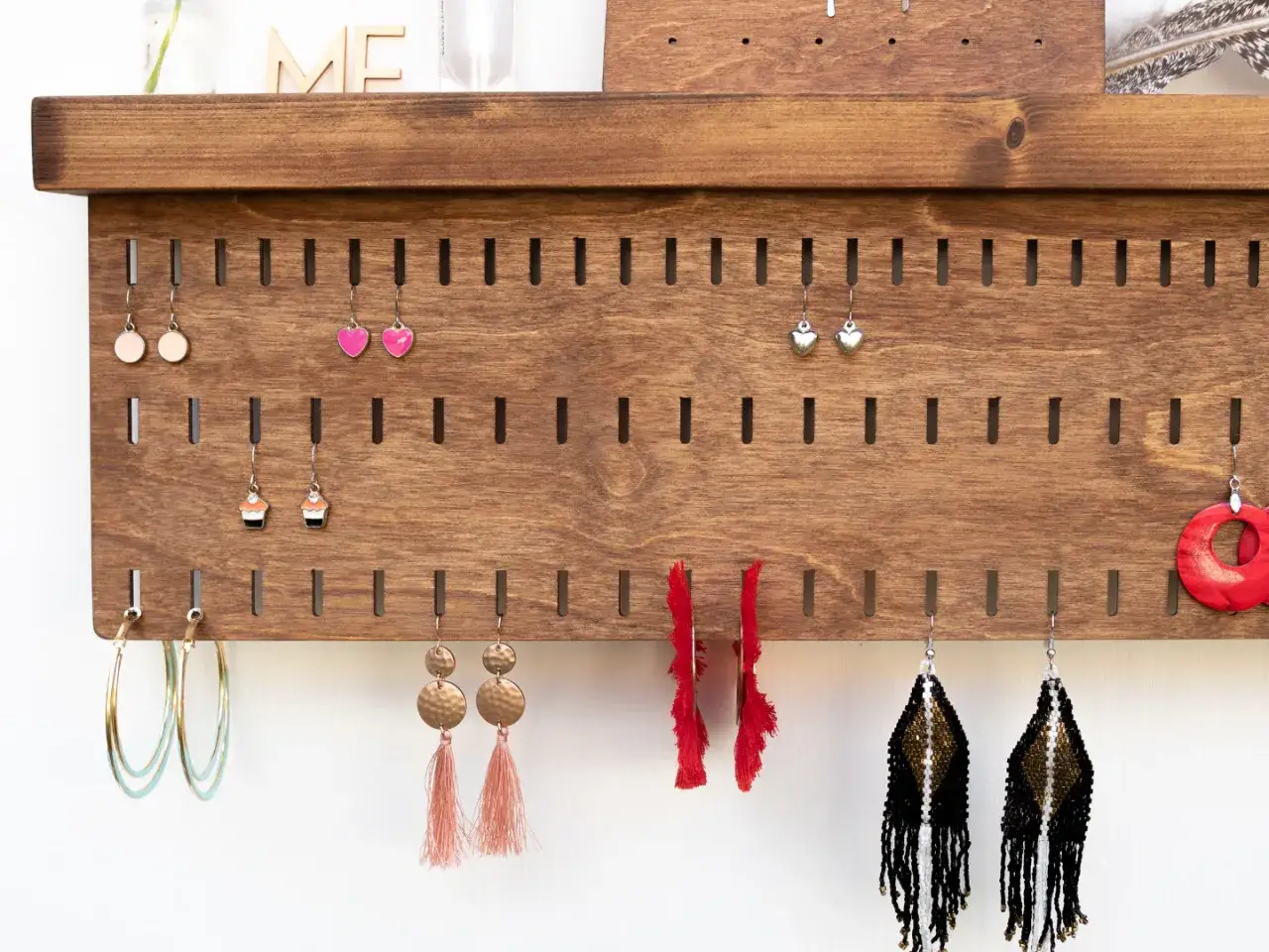 Holz-Organizer für Ohrringe, perfekt zum Ohrringe aufbewahrung selber machen. Viele bunte Ohrringe hängen an Schlitzen.