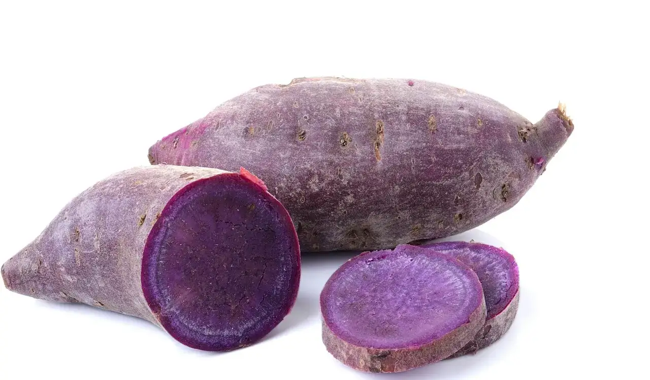 Lila batata, en s&ouml;tpotatis med intensiv f&auml;rg, skuren i skivor och halvor.