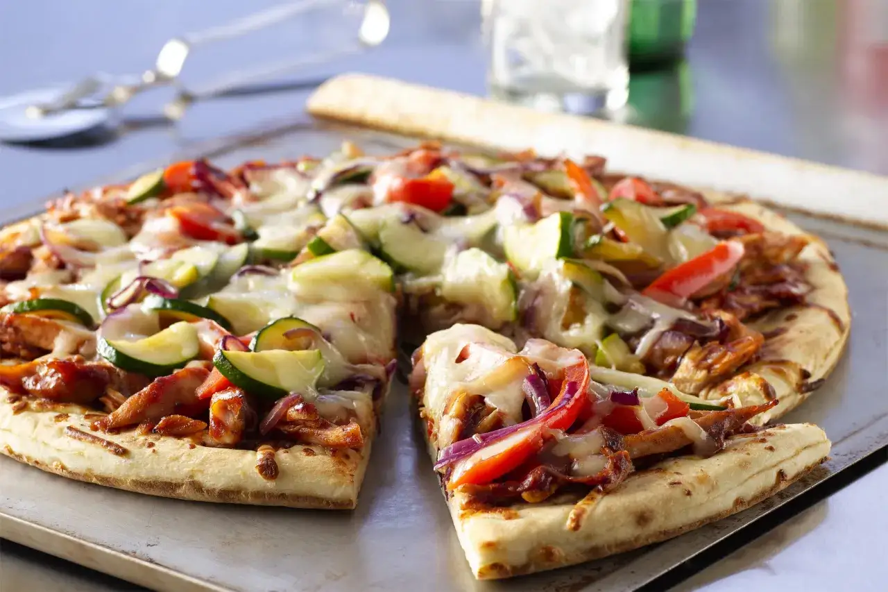 Pyszna pizza z kurczakiem, cukinią i czerwoną cebulą, obficie posypana ciągnącym się serem.