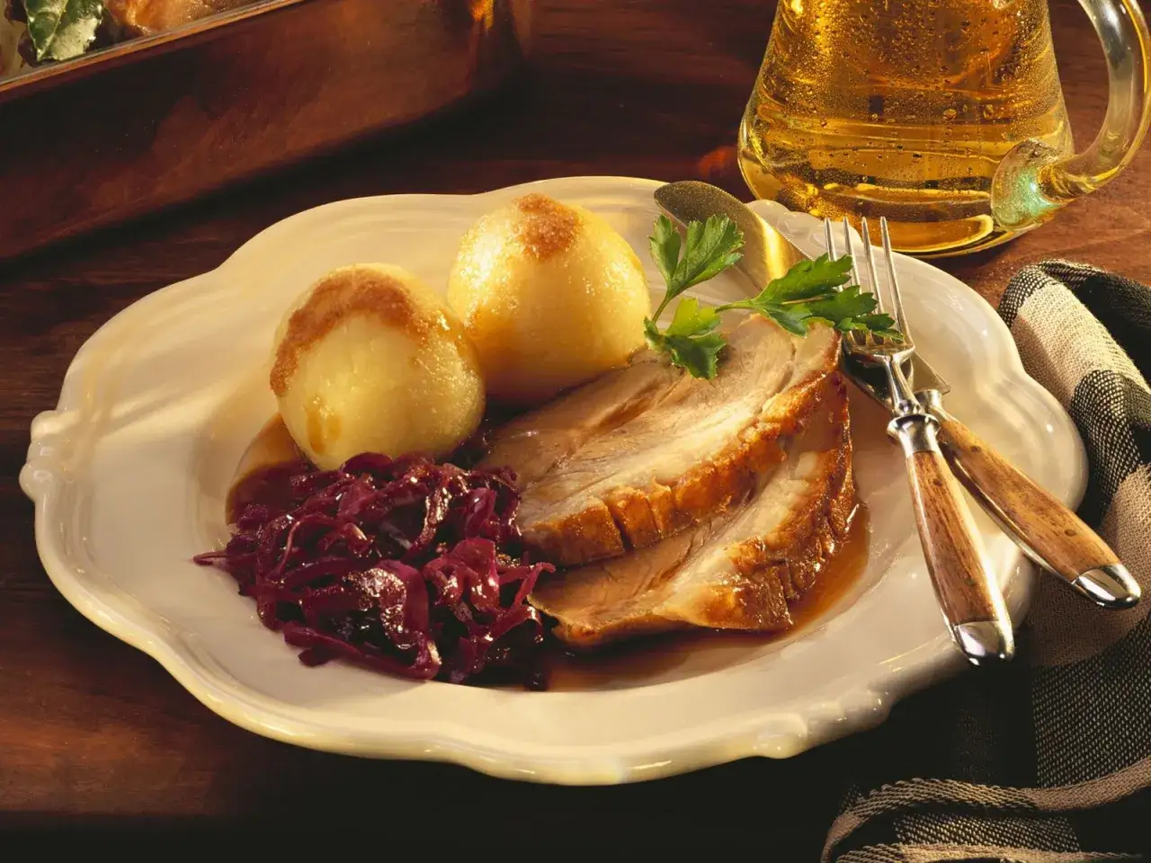 Deftiges Fleisch zu bayrisch Kraut mit Klößen, garniert mit Petersilie, daneben ein Bierkrug.