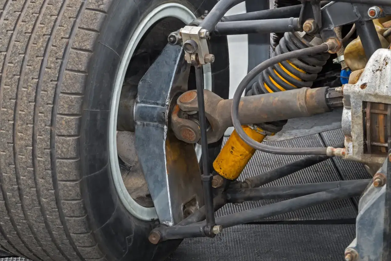 Gros plan sur la suspension d'une voiture de course, avec un pneu us&eacute;, un amortisseur jaune et le cardan. Le changement cardan prix est une pr&eacute;occupation pour les propri&eacute;taires.