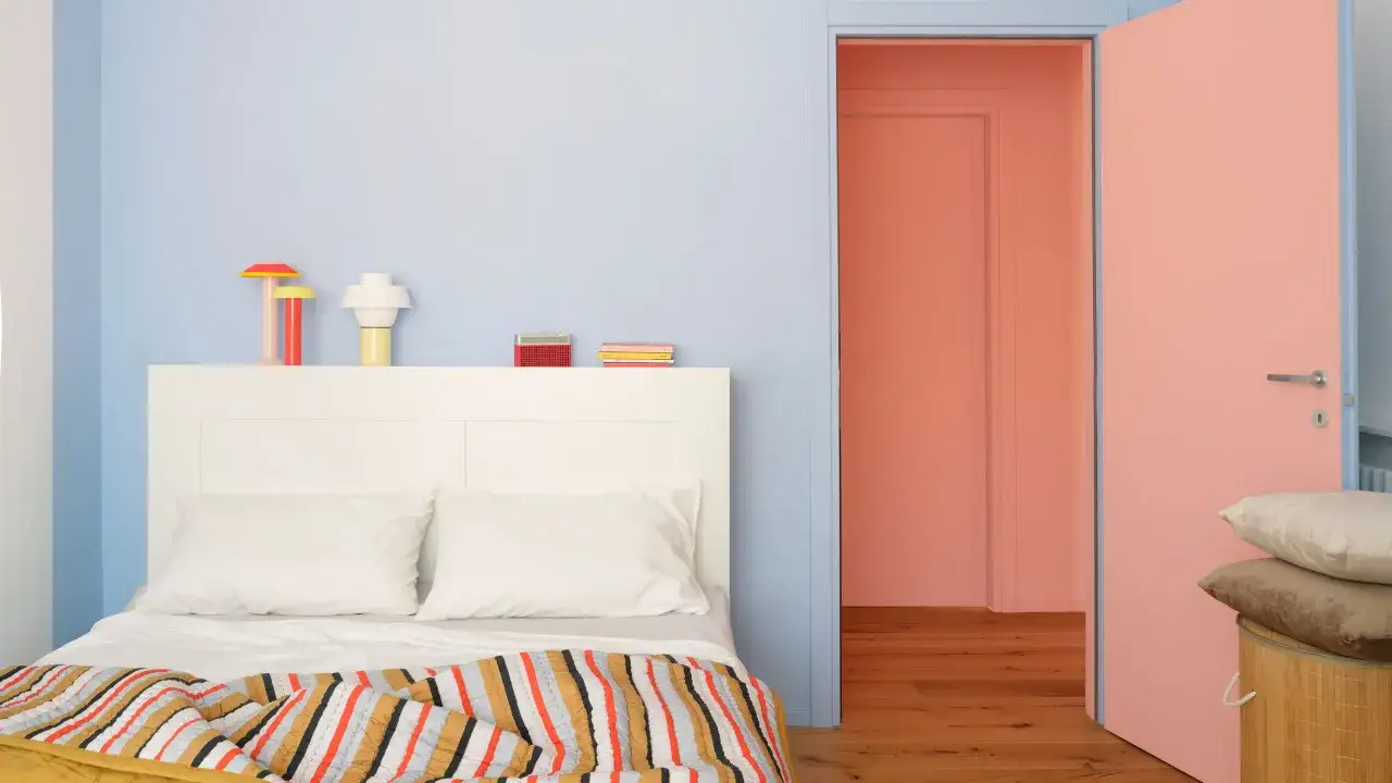 Chambre aux murs bleu pâle et rose corail. Quel mur peindre en couleur ? La porte ouverte sur un couloir rose invite à la couleur.