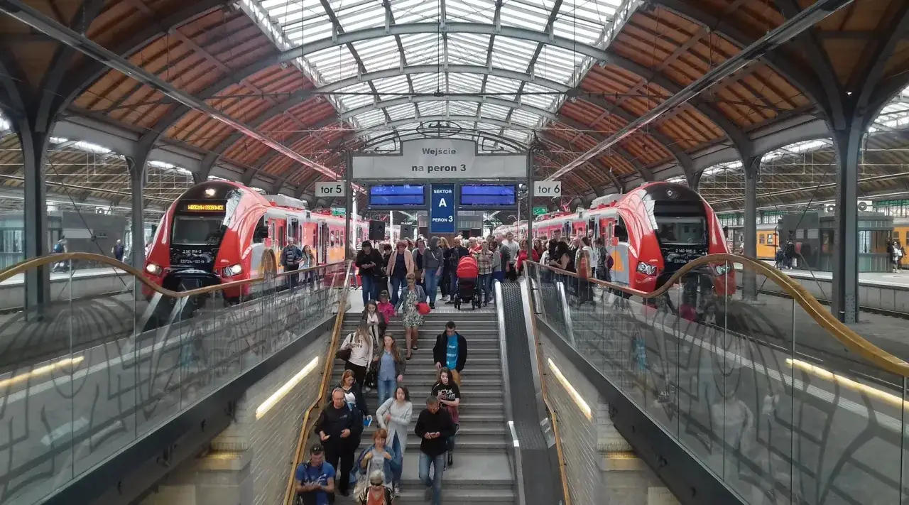 Ludzie schodzą po schodach na peron, gdzie czekają czerwone pociągi. Koleje PR w ruchu.