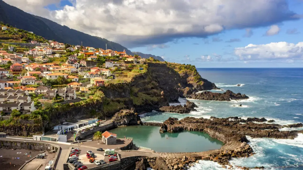 Bunte H&auml;user schmiegen sich an steile H&auml;nge auf den Inseln bei Madeira. Ein nat&uuml;rlicher Pool aus Lavafelsen l&auml;dt zum Baden ein, w&auml;hrend das Meer tobt.