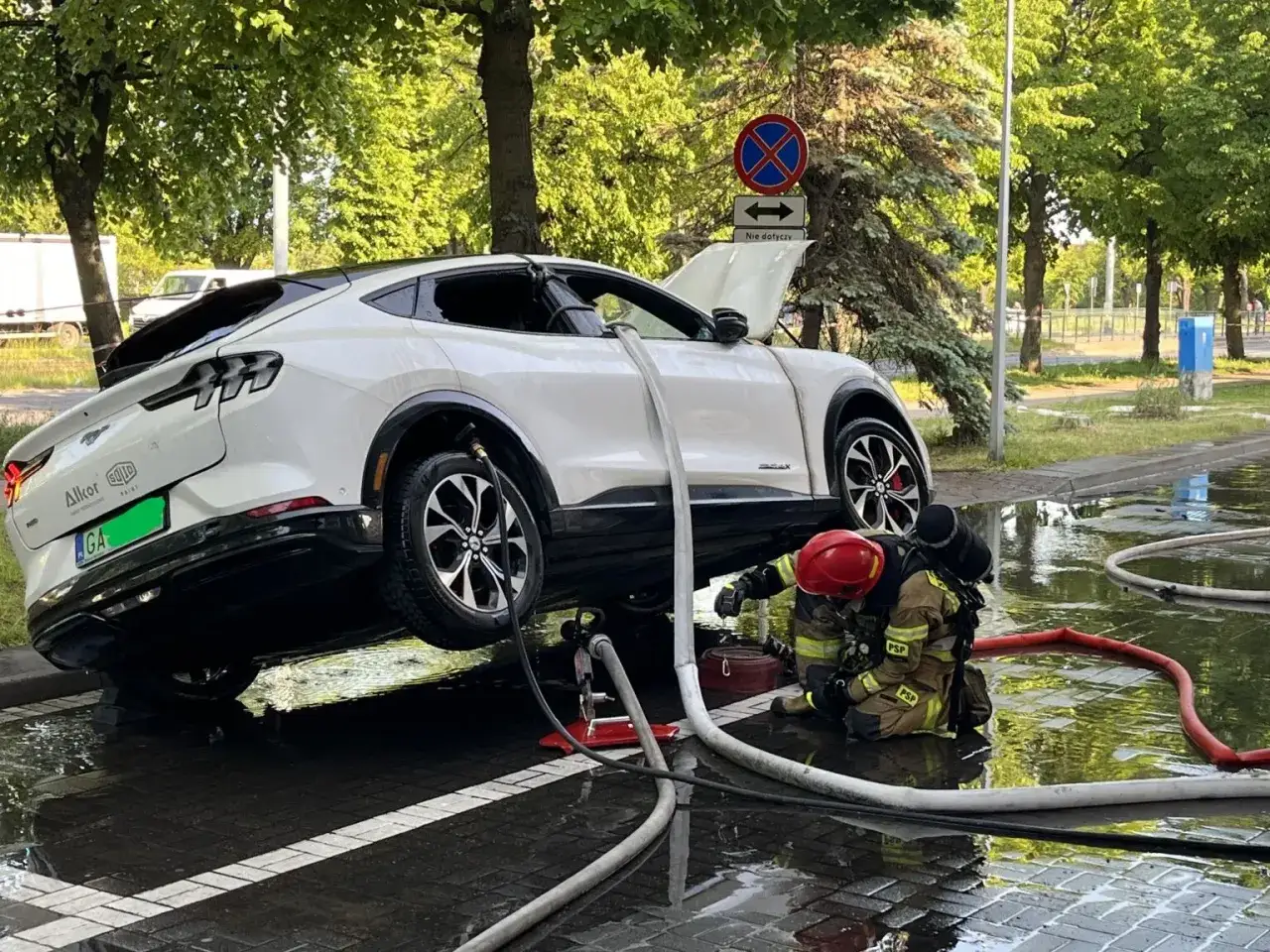 Strażak walczy z ogniem pod białym elektrycznym autem. Czy to zapowiedź, dlaczego w 2026 r. wzrosła liczba pożarów w warsztatach przez błędy w ładowaniu baterii?