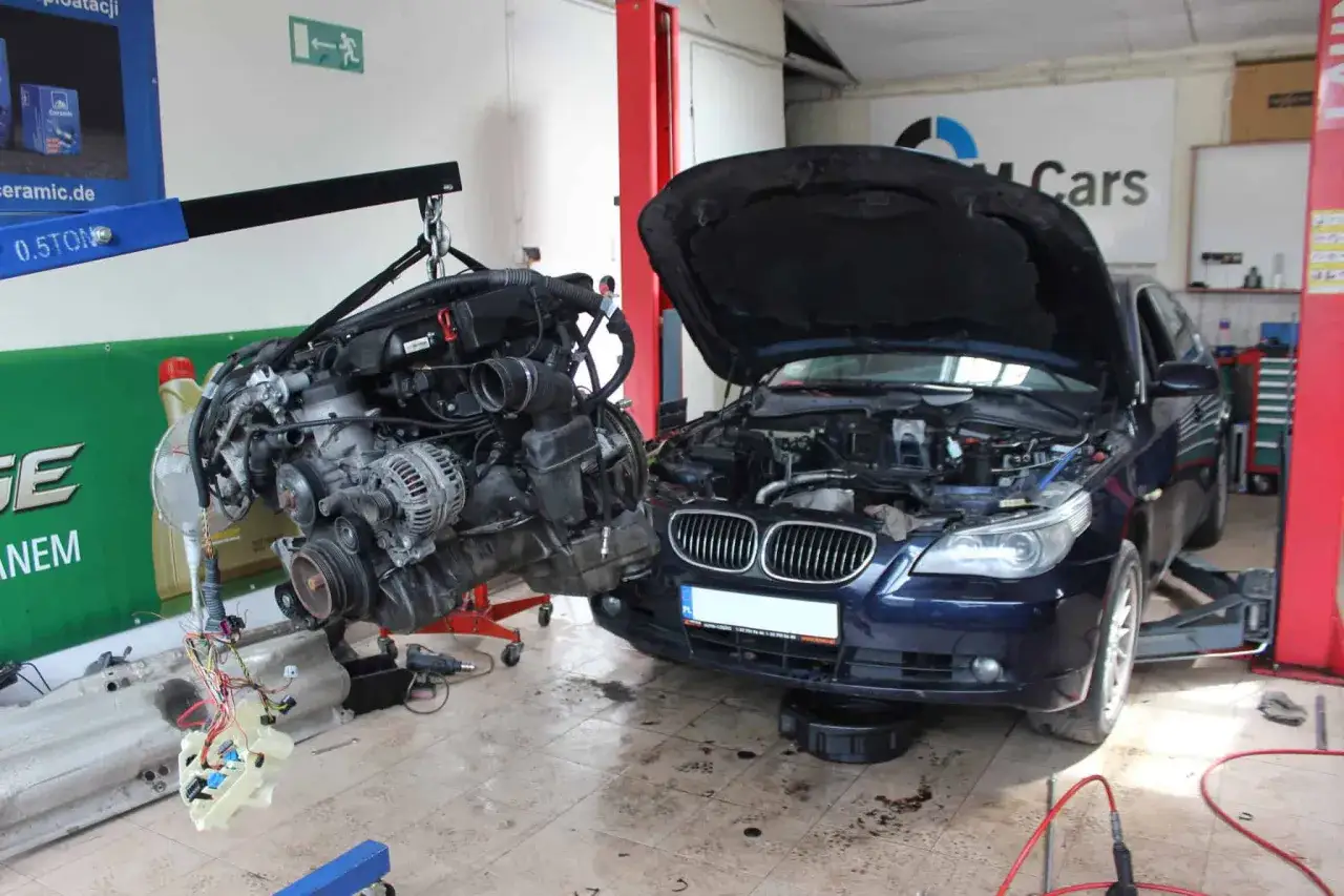Warsztat samochodowy, gdzie silnik BMW jest wyciągany. Zastanawiasz się, ile kosztuje robocizna wymiany silnika?