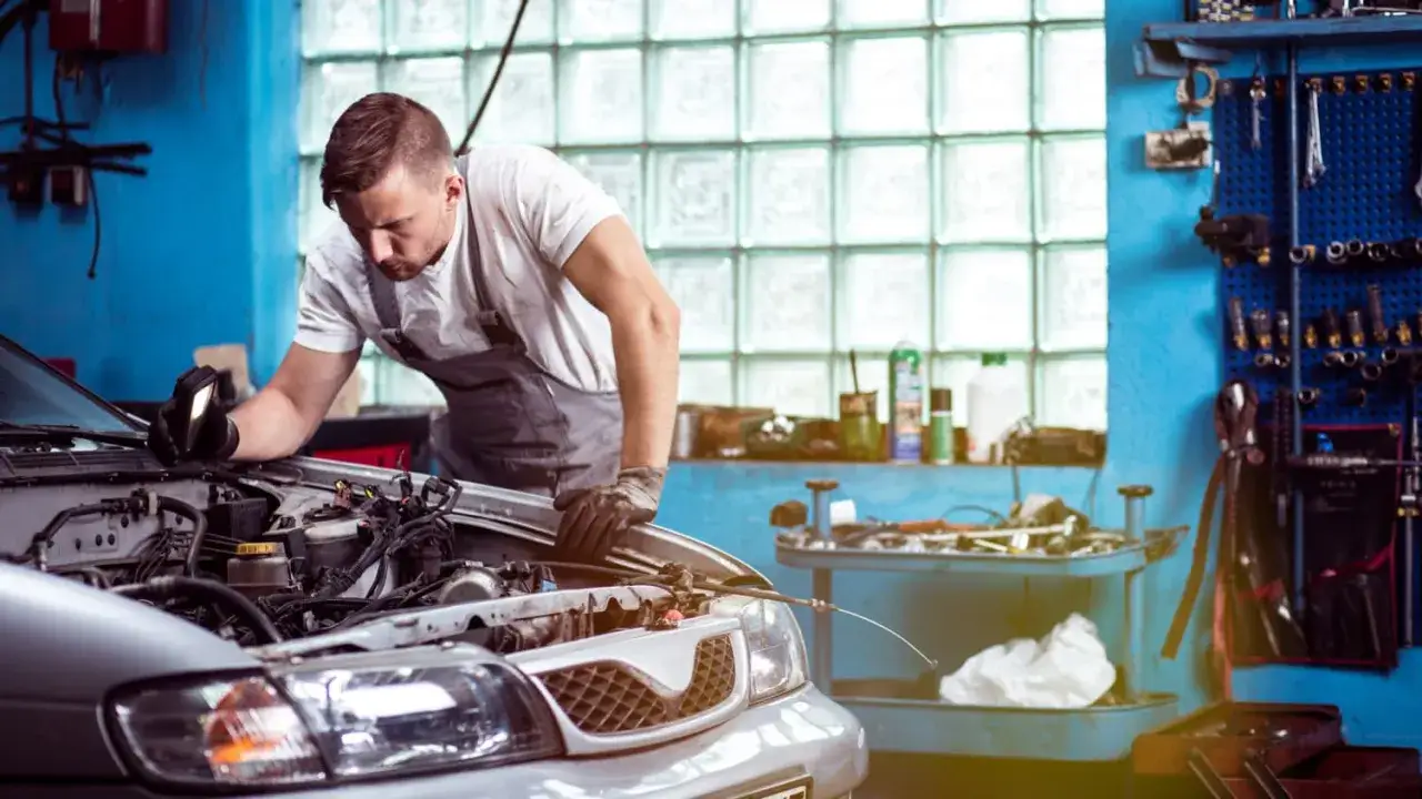Mechaniker untersucht Motor, frustriert, weil das Auto nach Reparatur wieder defekt ist. Werkstatt mit Werkzeugen im Hintergrund.