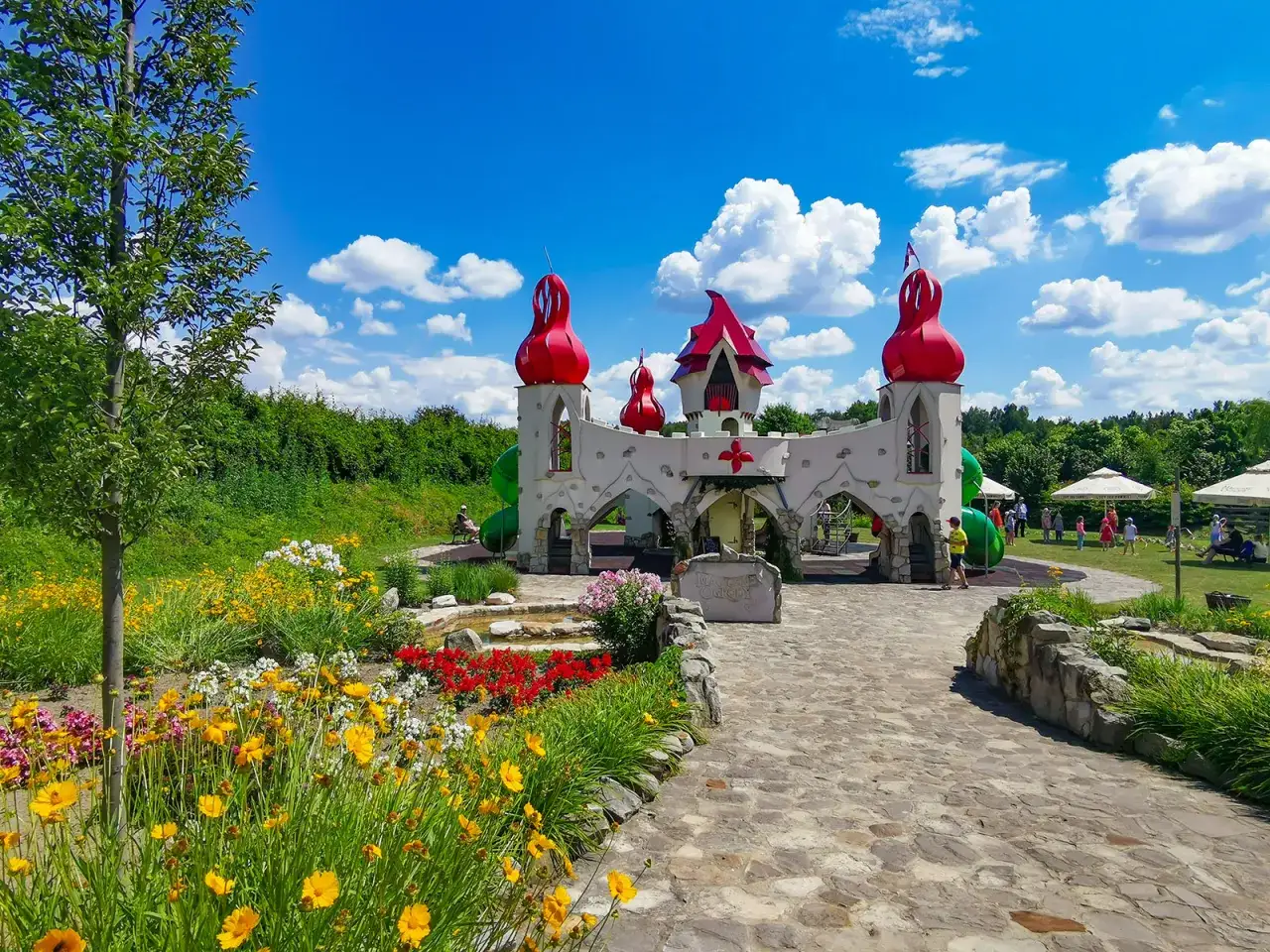 Kolorowy zamek z czerwonymi wieżyczkami i kwitnące kwiaty zapraszają do magiczne ogrody atrakcje.