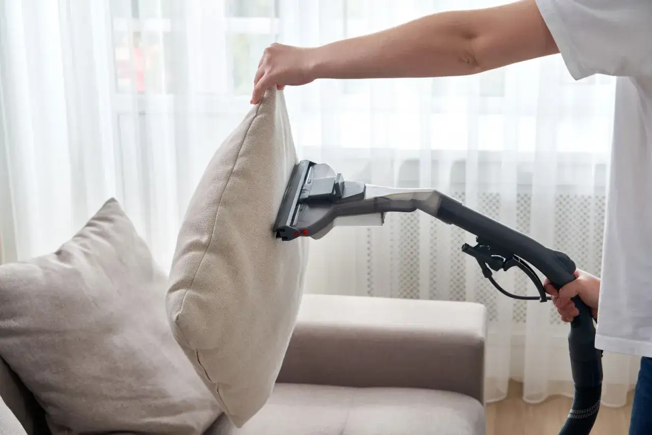 Person anv&auml;nder en soffdammsugare f&ouml;r att reng&ouml;ra en kudde p&aring; en soffa.