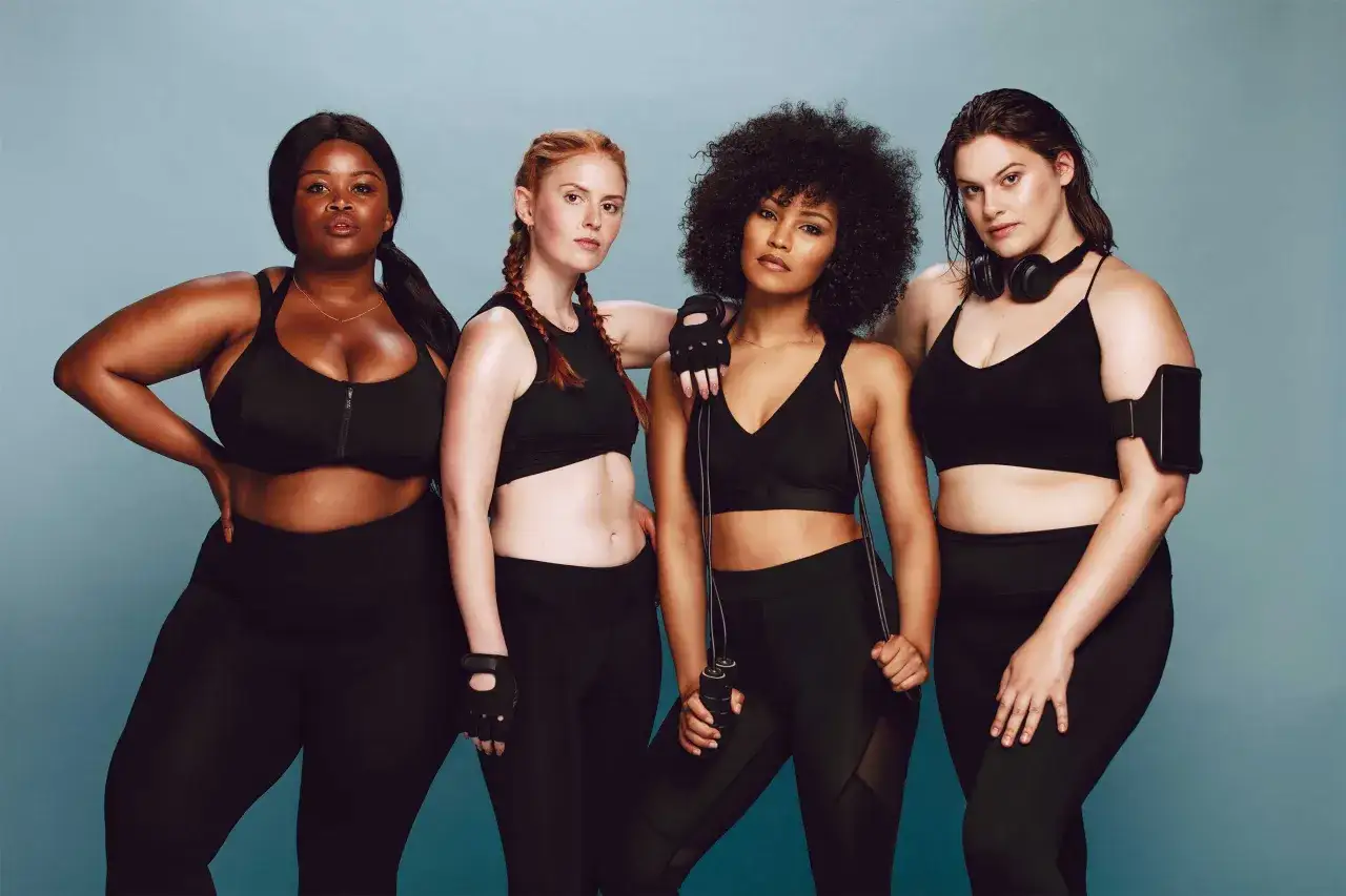 Quattro donne diverse, pronte a come allenarsi in palestra. Indossano abbigliamento sportivo nero, alcune con accessori come cuffie e corda per saltare.