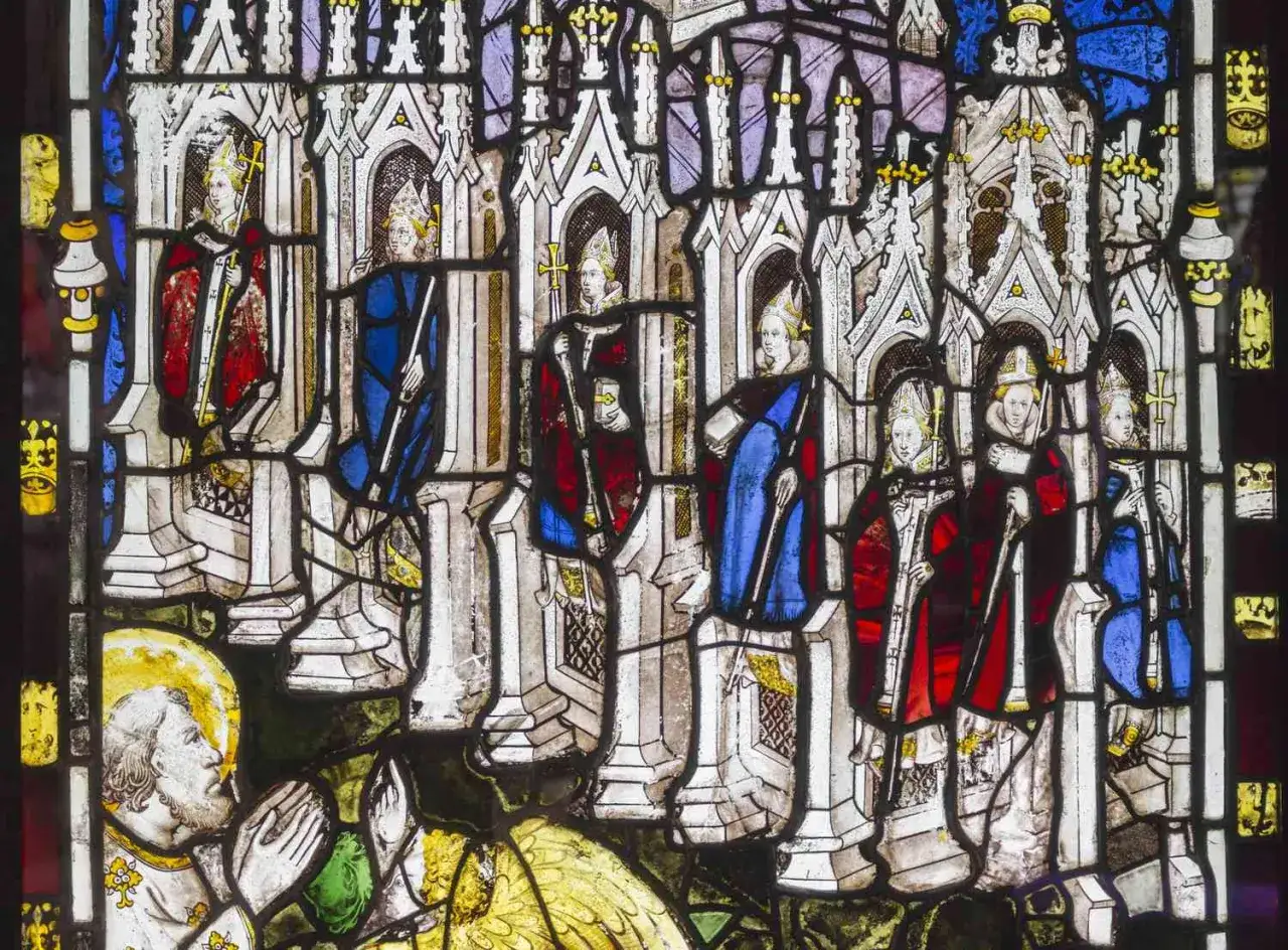 Stained glass figures in York Minster, depicting clergy in ornate robes and mitres, stand before architectural niches.
