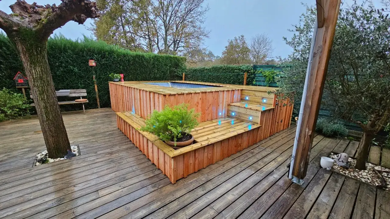 Aménagement abord piscine hors sol en bois avec éclairage LED bleu intégré. Un escalier mène à la piscine, entourée d'une terrasse en bois.