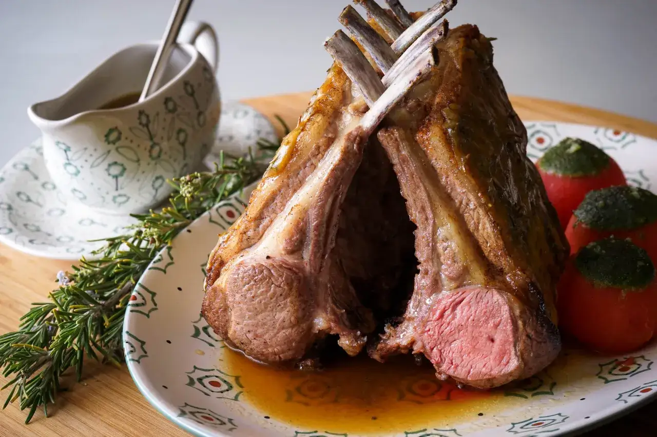 Un appétissant carré d'agneau rôti, servi avec des tomates garnies et une saucière décorée.