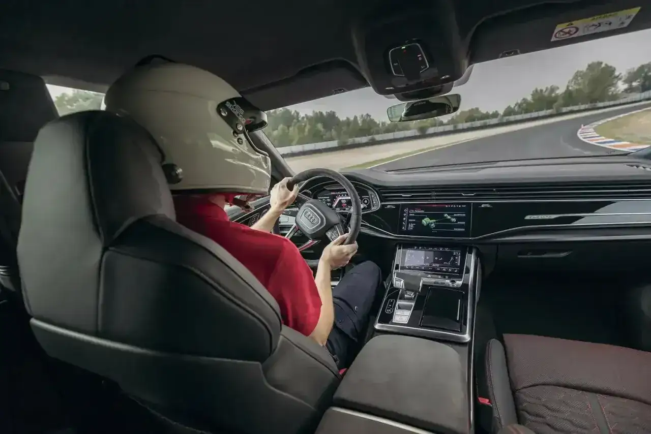 Kierowca w kasku za kierownicą Audi RS Q8 na torze wyścigowym. Sprawdź aktualną audi rsq8 cena i poczuj moc.