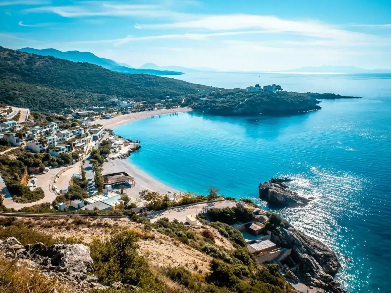 Malownicza zatoka z turkusową wodą, białe domki i plaża. Idealne miejsce na albania camping nad morzem.