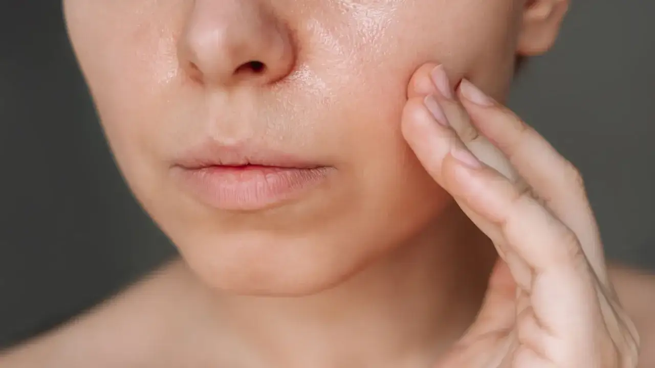 Delikatna skóra z widocznym **sebum**, dotykana palcami.