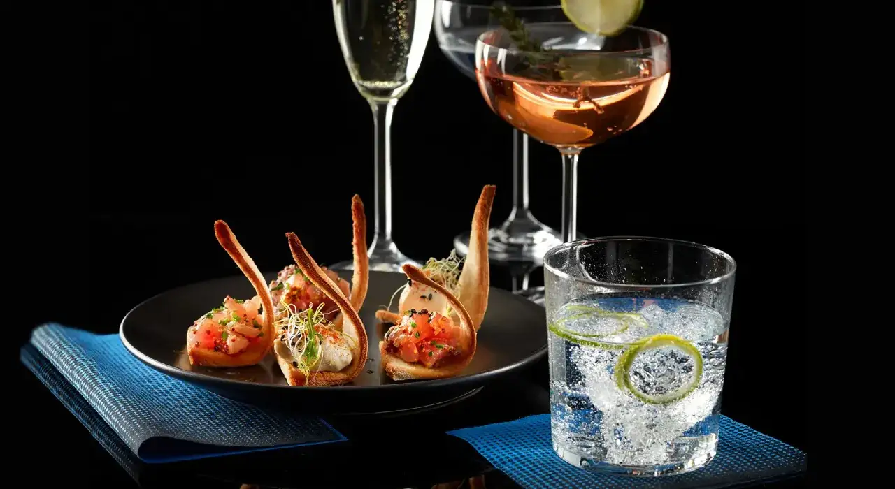 Eleganckie aperitif przykłady: tartare z łososia w kruchych łódeczkach, kieliszki z szampanem i różowym winem, drink z limonką.