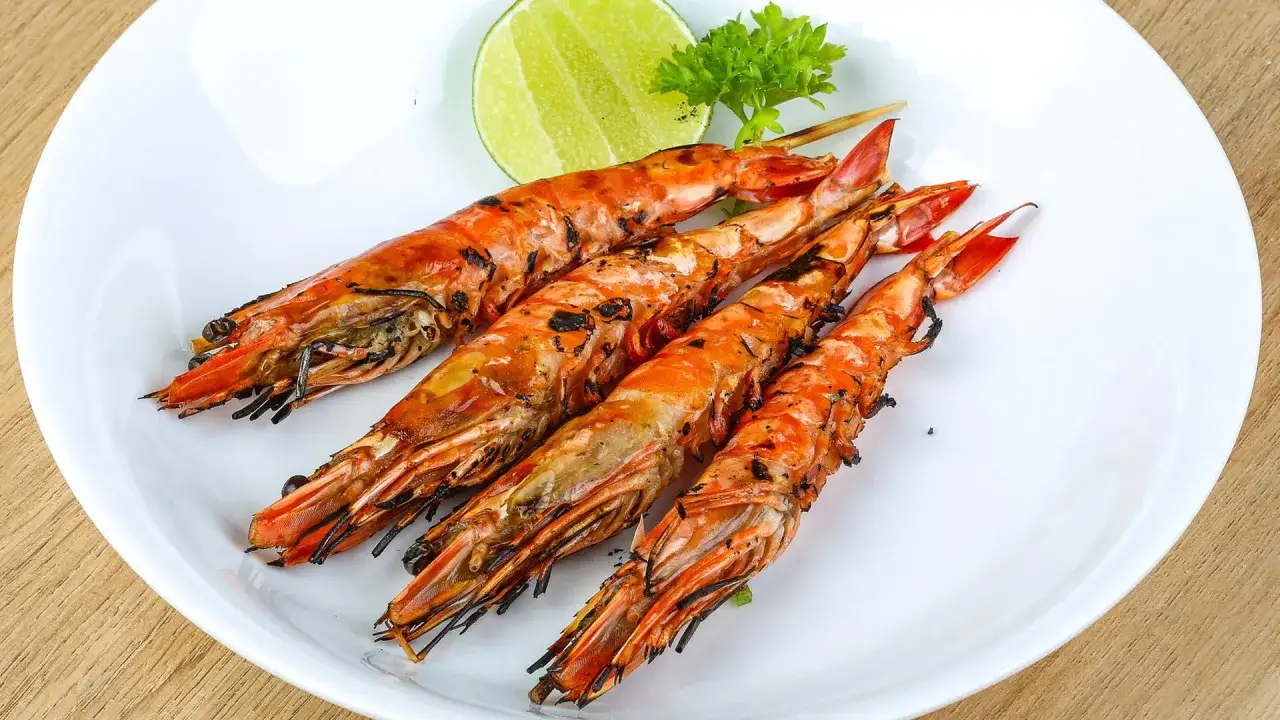 Cuatro langostinos a la plancha, dorados y jugosos, servidos en plato blanco con rodaja de lima y perejil.
