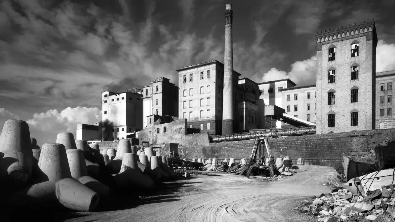 Un'architettura industriale imponente, quasi metafisica, con una ciminiera svettante e blocchi di cemento a forma di tetrapodi.