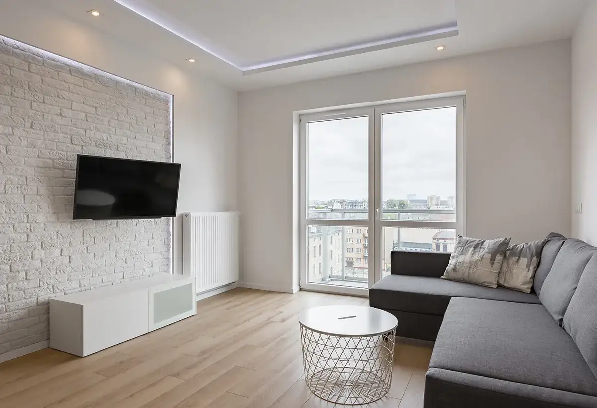 Salon moderne avec TV murale. La **norme hauteur TV par rapport au sol** est respectée pour un confort visuel optimal. Canapé gris, table basse et parquet clair.