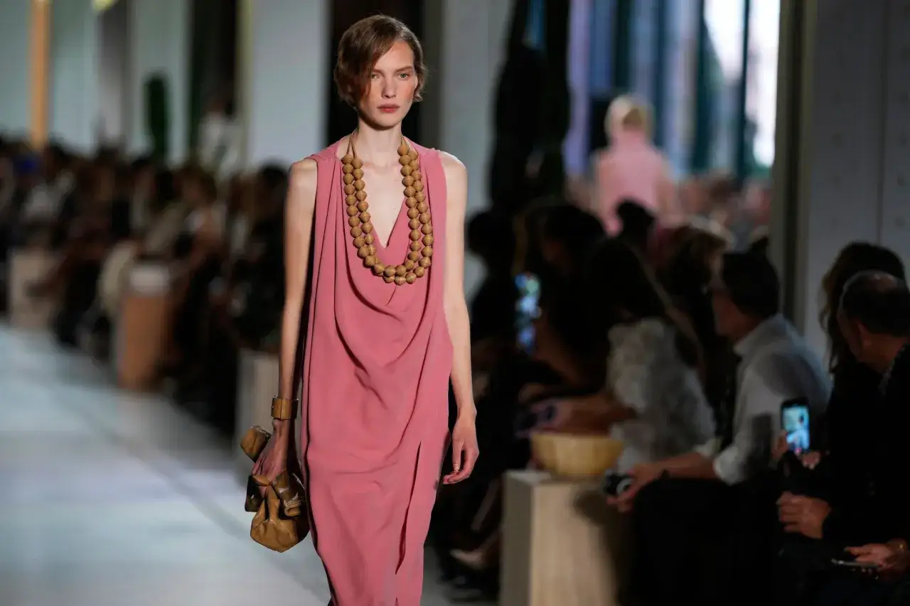 Modelka prezentuje różową sukienkę i brązową torebkę. To styl, który mógłbyś zobaczyć u marki Michael Kors – co to za marka?