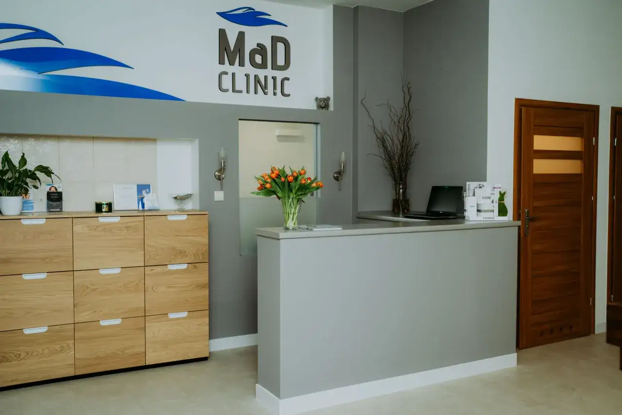 Recepcja kliniki MaD CLINIC z bukietem pomarańczowych tulipanów i drewnianymi meblami.